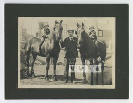 Portrait d’un homme se tenant près de ses fils alors qu’ils sont à dos de cheval dans un enclos