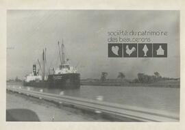 Un bateau de marchandises navigue sur un chenal, près d’une route